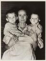 [Woman holding two toddlers in her arms]