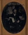 [Seated man holding paper]
