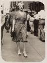 [Woman walking along sidewalk]