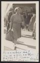 [Woman walking along sidewalk]