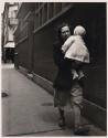 [Woman holding baby while walking down the street]