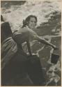 [Woman/model(?) on rocky shore with bucket]