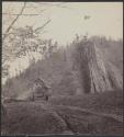 [Log cabins at base of rocky hill]