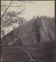 [Log cabins at base of rocky hill]