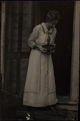 [Woman standing in door frame holding a camera]