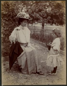 [Woman sitting in chair with young girl holding camera]