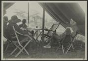George Eastman smoking cigarette in tent with companions, African Safari