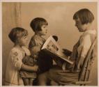 [Girl reading to two children]