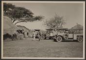 Osa Johnson conversing near automobiles and huts, African Safari