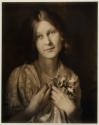 [Young woman wearing strand of pearls, clutching a fabric flower]