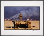 An American soldier stands on top of a destroyed Iraqi tank. Kuwaiti oil wells, ignited by Saddam's retreating forces, burn in the distance, Kuwait