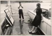 [Man taking home movie of woman, who leans against a car, on the Columbus ferry]