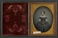 [Young woman, standing with hands crossed at front, hair-jewelry earrings]
