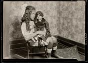 [Girl in a rocking chair holding a doll]