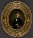 [Seated man leaning on book and table]