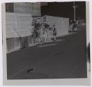 [Children playing on sidewalk near piles of wood planks]