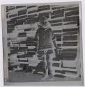 [Boy standing in front of a pile of wood planks]