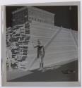 [Boy and girl standing beside a pile of wood planks]
