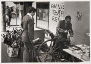 An umbrella repairman hammering and repairing a handle in the Basque town of Eibar, behind him are amnesty slogans and communist insignia, Spain