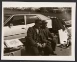 [Two men seated in front of car]