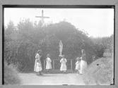 [Children and nuns at grotto with statue of Our Lady of Lourdes and large Crucifix]