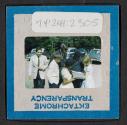 [People standing outside looking at a book (travel slide)]