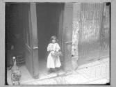 [Child in Doorway Holding Basket]