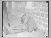 [Old Man Resting in Road Against Brickwall]