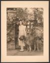 [Woman standing with dog in front of gate with roses]