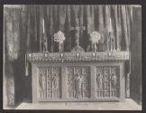 [Candlesticks, flowers, and cross on carved altar in church]