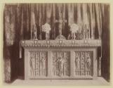 [Candlesticks, flowers, and cross on carved altar in church]