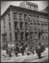 [Spectators on street corner watching policeman on ladder]