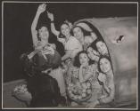 [Eight women sitting in covered structure with baskets of produce]