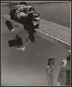 [Photographer with camera on diving board, two women in bathing suits at bottom of empty pool]