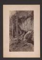 [Man sitting below rocky outcropping]
