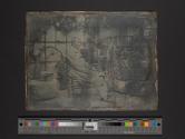 [Man seated in front of garden wall]