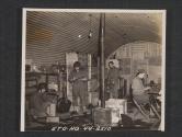 [A busy supply room of a unit in Northern Ireland. T/5 Willard Kephart, Homer, IND., checks in supplies with S/SGT John S. Charo, Cleveland, O. in the background PVT Colin Garug, Portland , ORE., is packing some "1x1'D" material. PVT Warren Hartman, Ann Arbor, MICH., types out a requisition,  5th Sig Co., 5th Inf Div, Braynsford, County Down, Northern Ireland.]