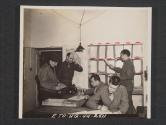 [The busy message center of a signal company in Northern Ireland. PFC Gerald Horton, Cleveland, Ohio, a signal corps photographer, hands a package of film to the counter clerk, T/5 Norbert Wendlandt, Milwaukee, WIS., S/SGT Bernard Halderson, Galesville, WIS. S/Asst message center chief is on the phone. PVT Jack Rosenbaum, Atlanta, GA., is Distributing messages while PVT Fred Oswald, Chicago, ILL., logs the messages in his dispatsh book.  5th Sig Co. 5th Inf Div, Braynsford, County Down, Northern Ireland. ]