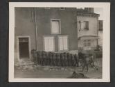 [Twelve Nazi prisoners seized during U.S. engagement in the Mozelle River sector near the Franco-German border are shown leadning against a house wall, hands over heads, while an armed guard stands watch over them prior to movement toward rear.]