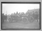 [auto racers surrounded by men at track]
