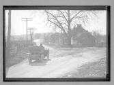 [auto on country road passing house]