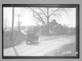 [auto on country road passing house]