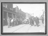 [auto racers surrounded by spectators in town "#63"]