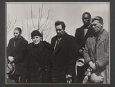 [Five men in dark coats standing with somber expressions.]