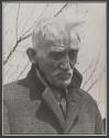 [Old man in coat with tree branches in background on the set of the film "Native Land."]