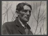 [Tall man in coat with tree branches in background, on the cemetery set of the film "Native Land."]