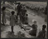 [American man and woman watching Mexican women and children do laundry by river]