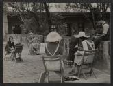[Four women and a man drawing a girl standing next to a wall with a shawl around her head and a basket of flowers at her feet]