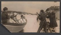 [Two men photographing children in boat on beach]