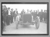 [auto racers surrounded by spectators]